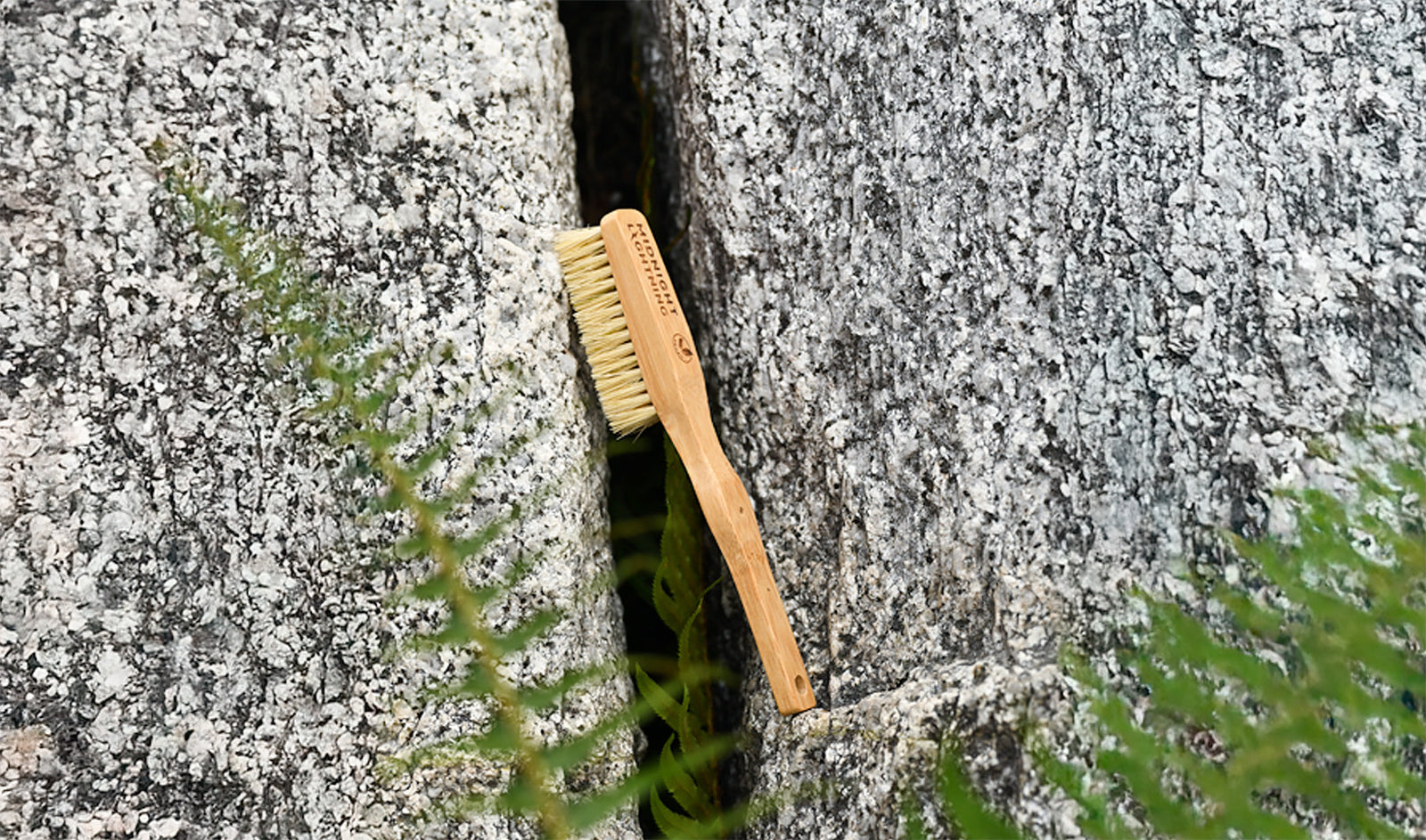 Vegan climbing brush with sisal bristles and bamboo hanfle leaning against rock with foliage in foreground