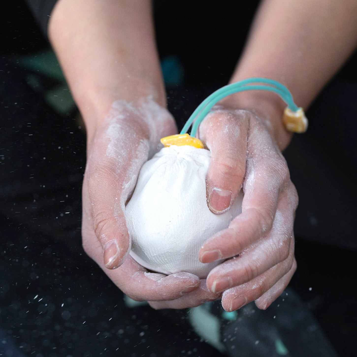 A cylindrical container labeled "Packaged Chalk Sock by Midnight Lightning" holds a refillable chalk sock, used for climbing or gym activities. The sock is white with yellow and teal pull strings. The container's design includes a lightning bolt symbol and teal and yellow color scheme.