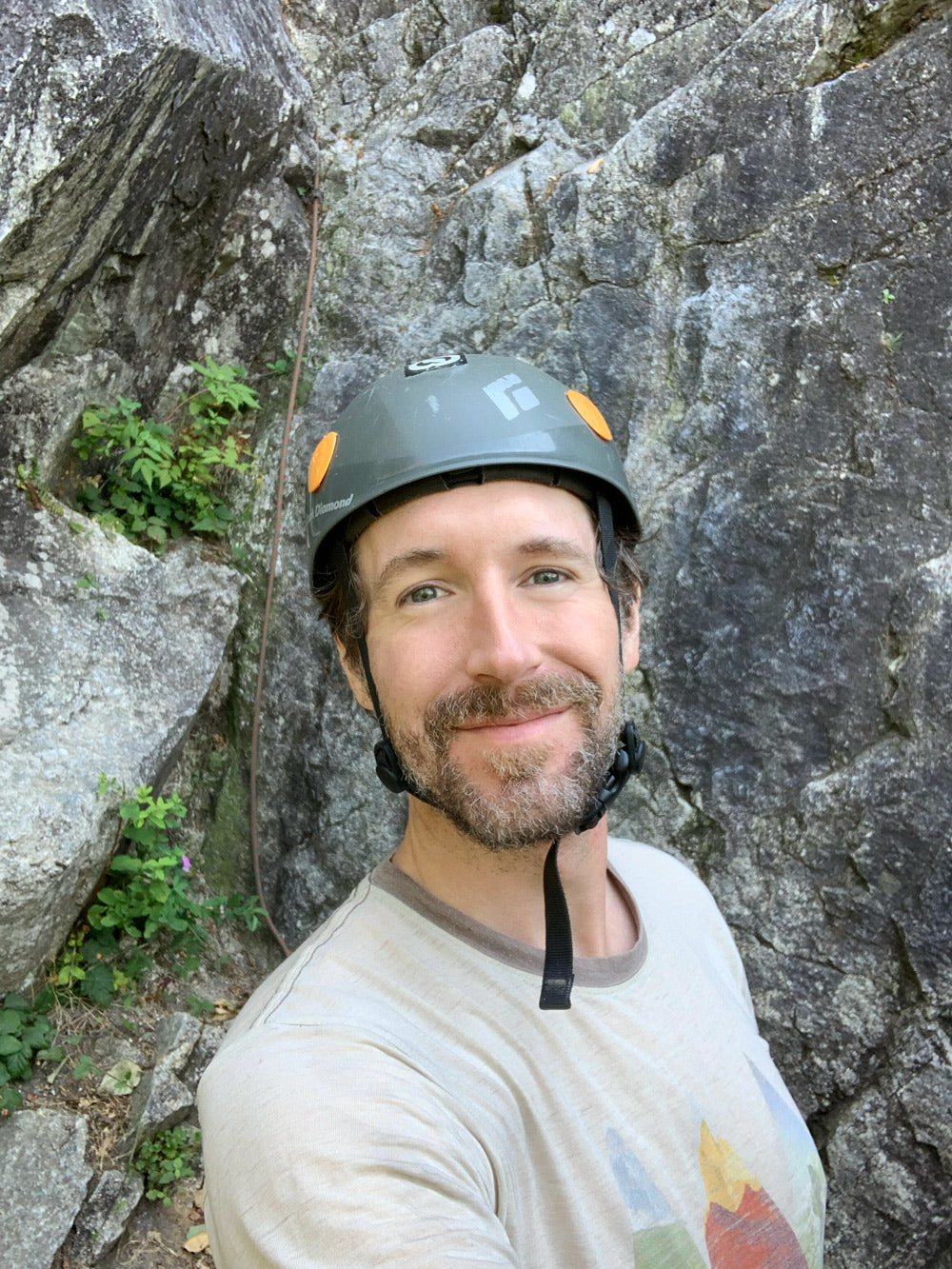 Midnight Lightning founder, Jon Thorpe, posing with a smile with a climbing helmet on his head. A climbing route fills the background. 